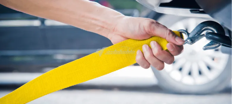 Рука тримає жовту стрічку для буксирування автомобіля.