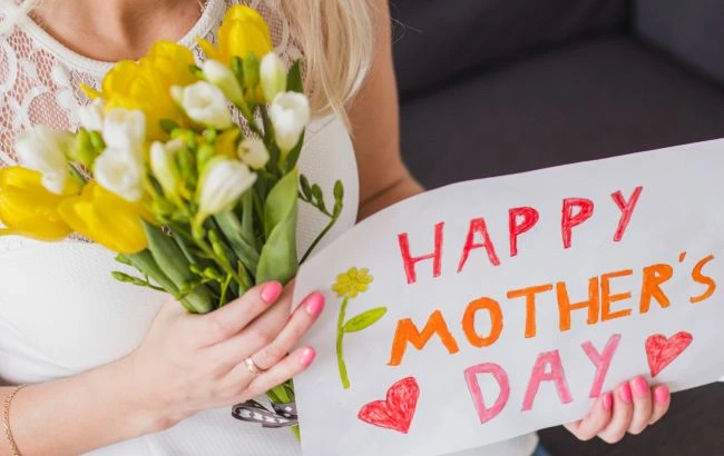 Дівчина тримає букет жовтих квітів та напис «Happy Mother’s Day».